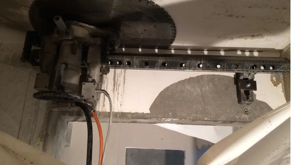 Une scie murale hydraulique professionnelle montée sur un système de chenilles coupant une structure en béton.
